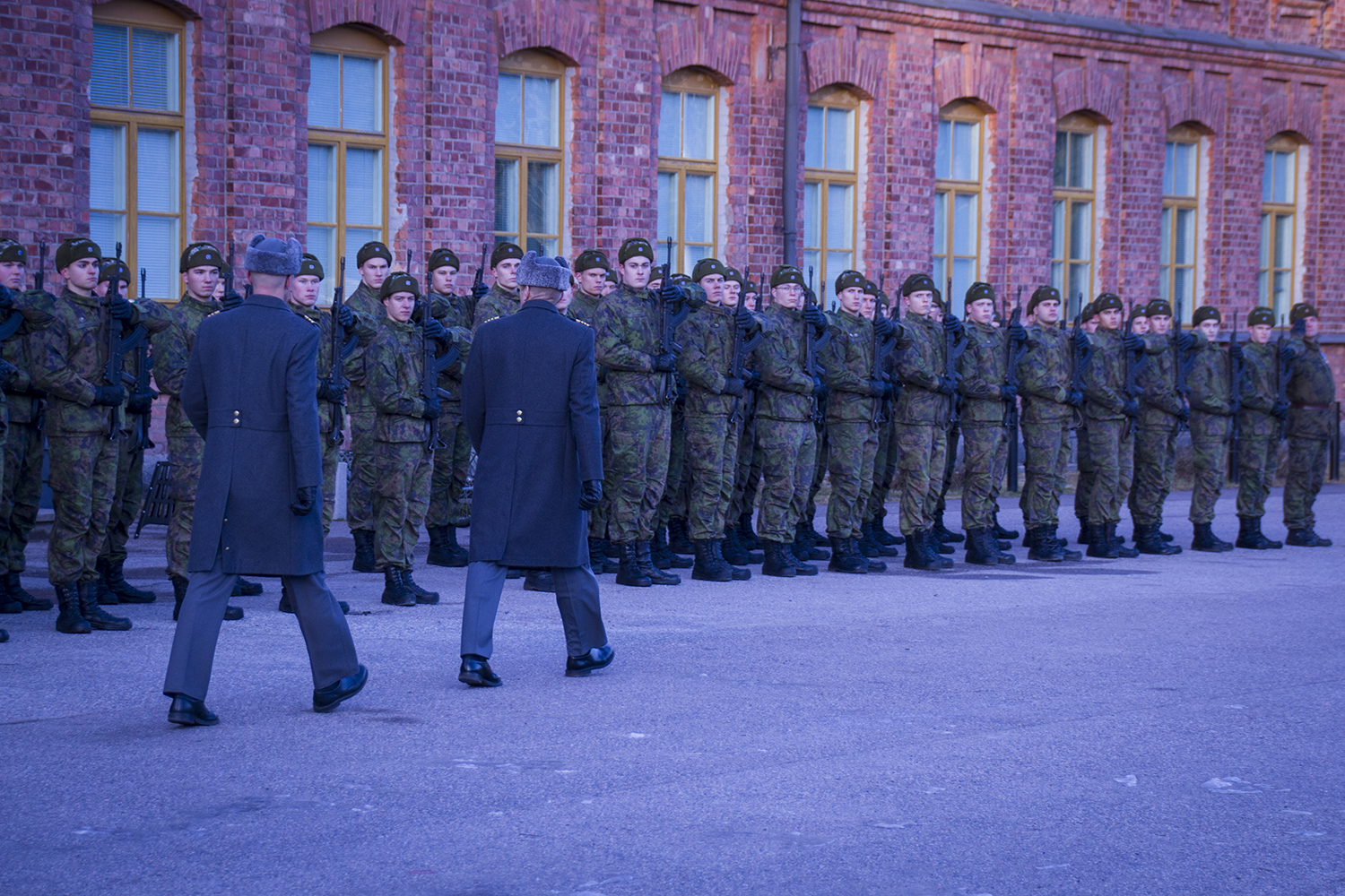 Varusmiehet seisovat muodossa rynnäkkökiväärit eteen vietynä kun komentaja marssii heidän edestä ja tarkastaa joukot