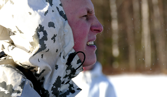 Lumipukuinen sotilas siristää silmiään auringossa